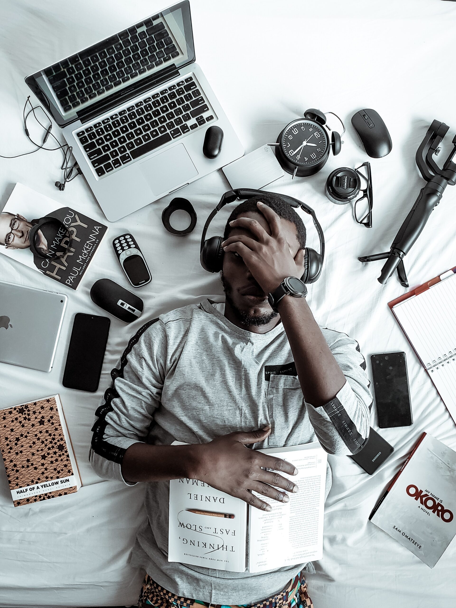 Person laying on a bed while wearing headphones, surrounded by items commonly found in a workplace office.