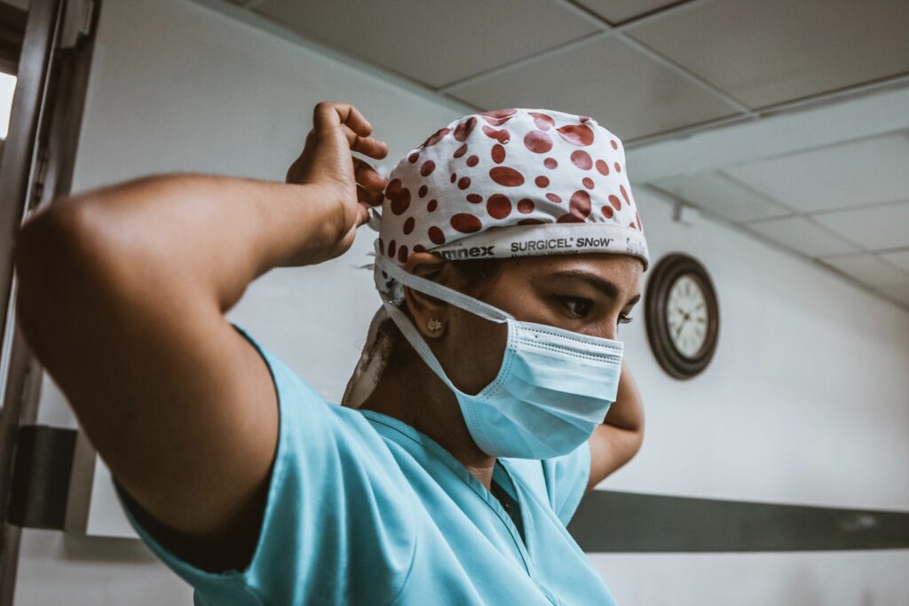 A person in scrubs ties on a face mask